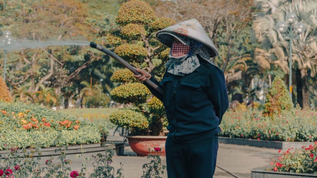 photo of a man wearing a pointed hat and protection mask spraying pesticides in a garden